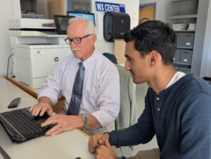 Senior meteorology student Cameron Kurasz helps Neal Macmillen prepare a PowerPoint for his forecast.